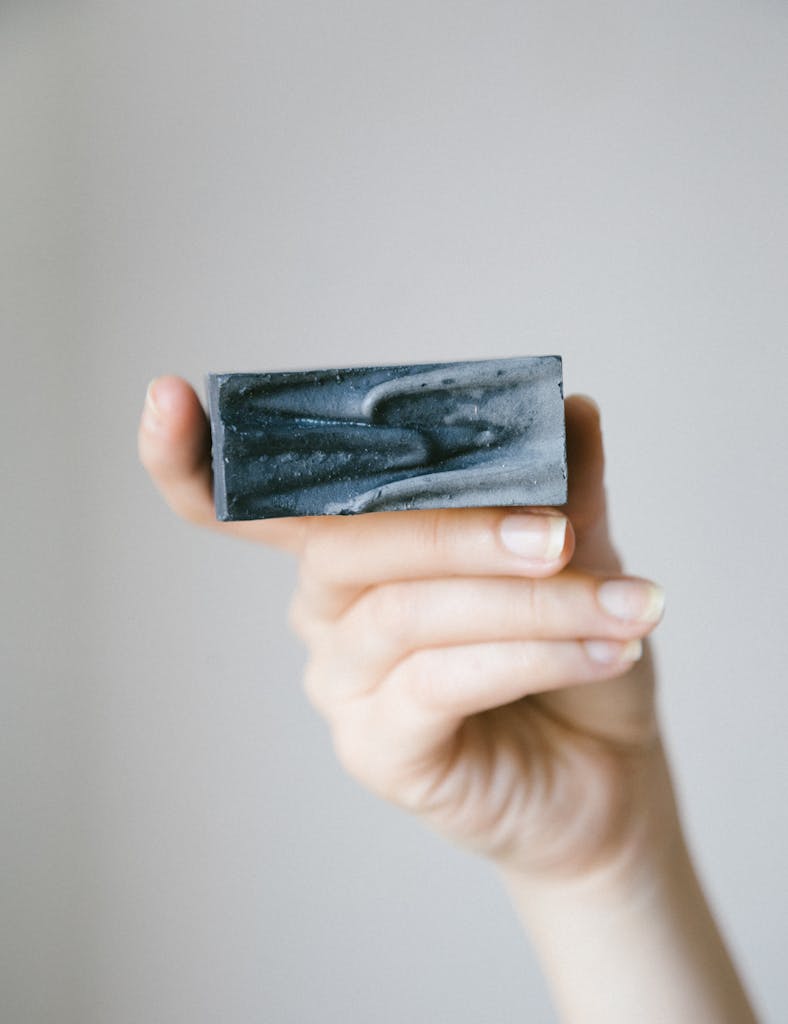 Close-up of a hand holding a black soap bar with a minimalist background.