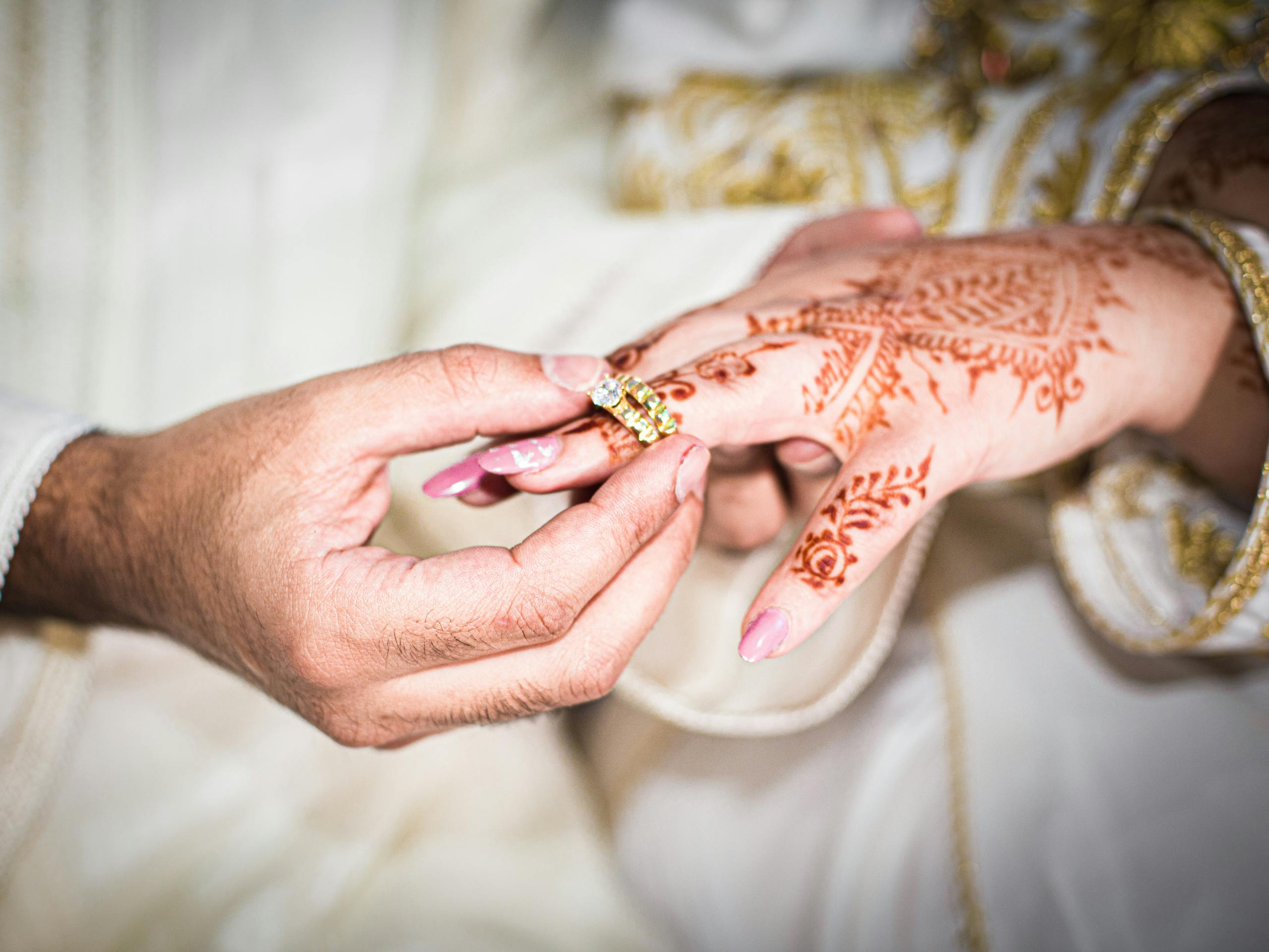 Close-up of an engagement ring exchange with henna tattoos in a traditional wedding setting.