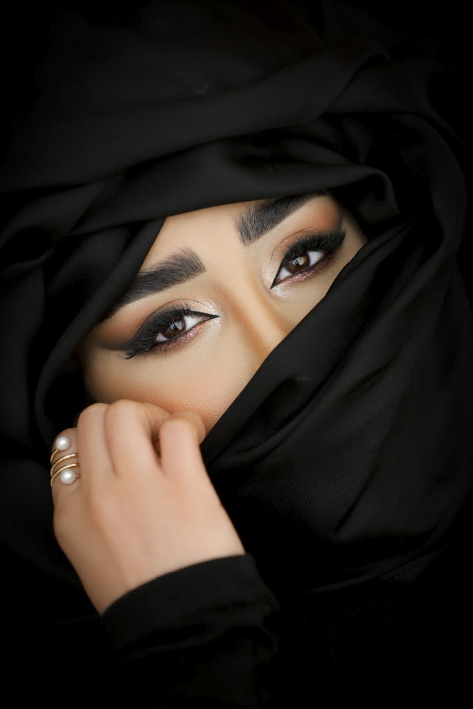 Close-up portrait of a woman with striking eyes wearing a black hijab.